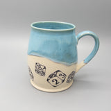 Ceramic mug with blue top and beige bottom featuring dice designs on a gray background