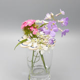 Clear glass vase with a bouquet of pink, purple, and white flowers on a gray background